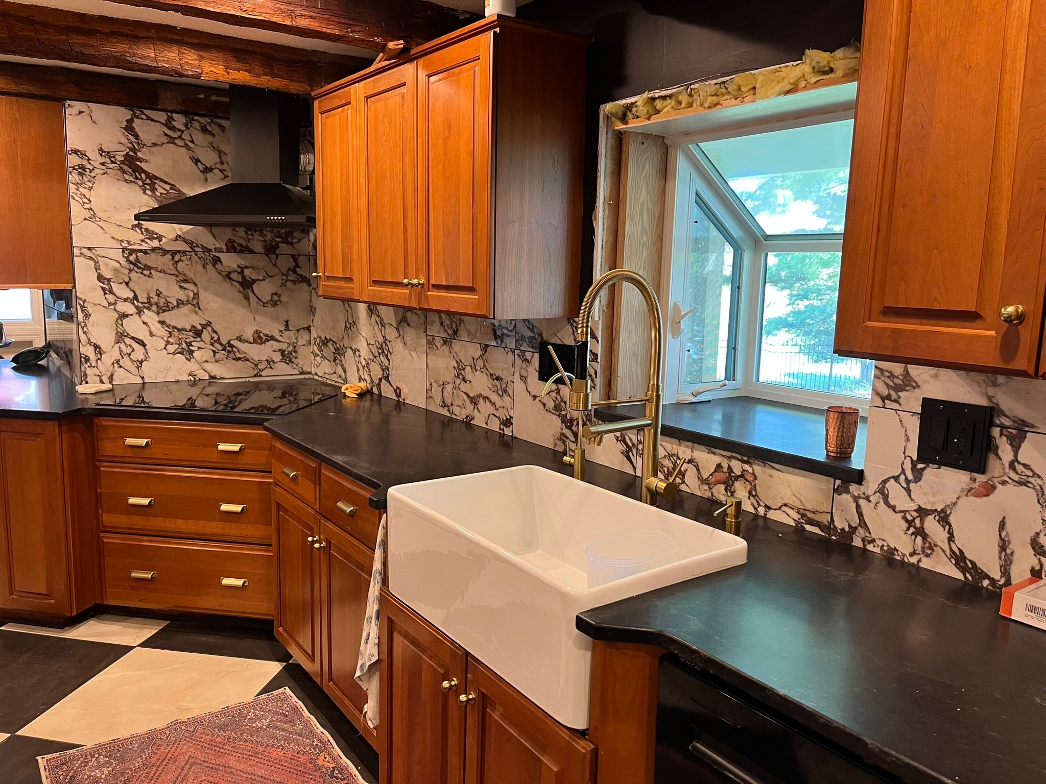 Kitchen with black soapstone countertops, marble backsplash, and farmhouse sink